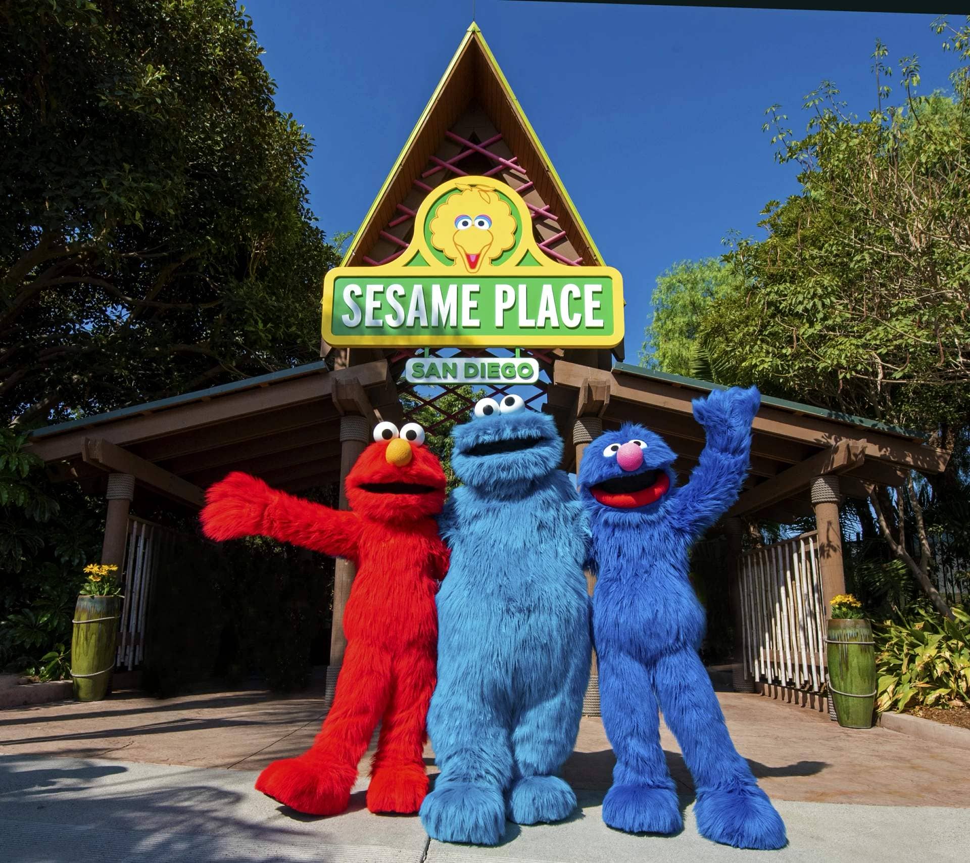 Elmo, Grover, and Cookie Monster stand in front of the entrance to Sesame Place San Diego.