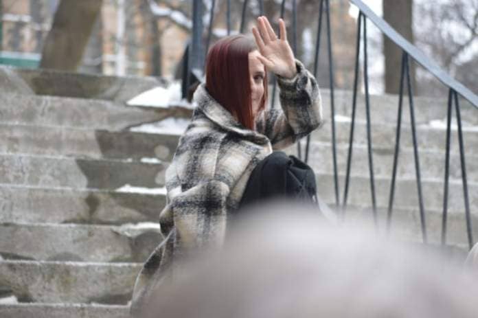 A woman waves and smiles on steps outside