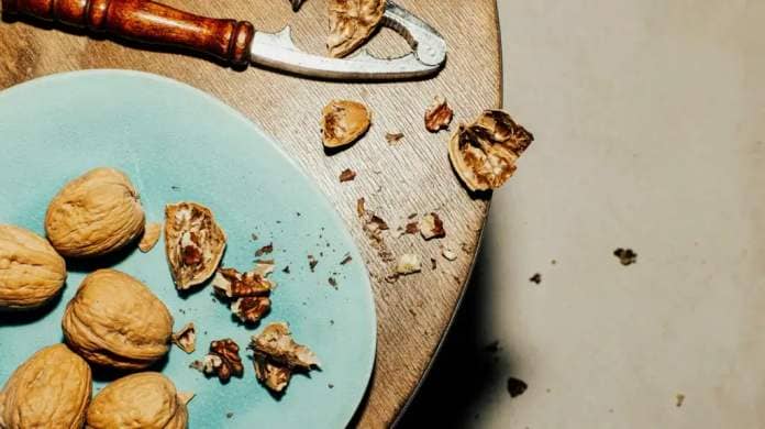 walnuts on blue plate next to nutcracker on wooden table