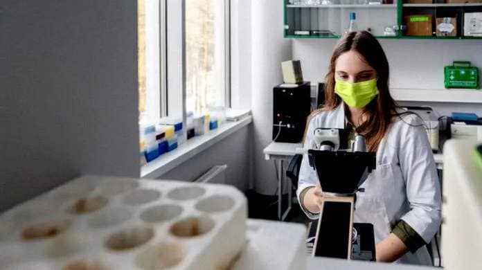 researcher wearing green face mask looking through microscope