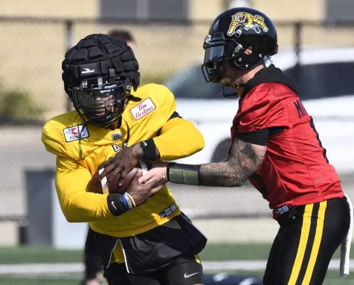 Ticat quarterback Bo Levi Mitchell hands off to running back James Butler, who is wearing a Guardian Cap, a soft-shell helmet cover.