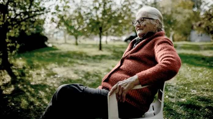 An older woman sits in a chair outdoors