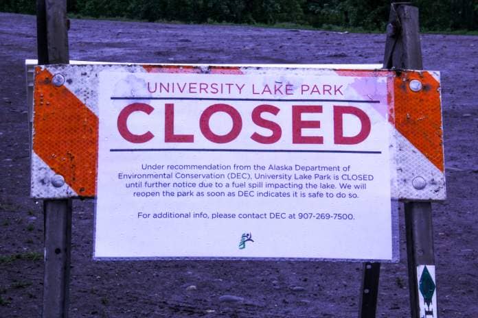 A sign that reads "University Lake Park CLOSED. Under recommendation from the Alaska Department of Environmental Conservation (DEC), University Lake Park is CLOSED until further notice due to a fuel spill impacting the lake. We will reopen the park as soon as DEC indicates it is safe to do so. For additional info, please contact DEC at 907-269-7500."