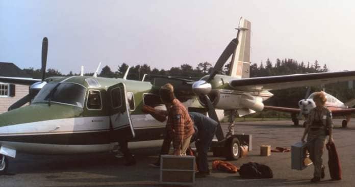Three people load boxes onto a small, green propeller plane.