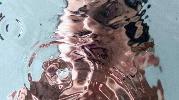 The reflection in water of a woman washing her face, the image blurred by a drop of water