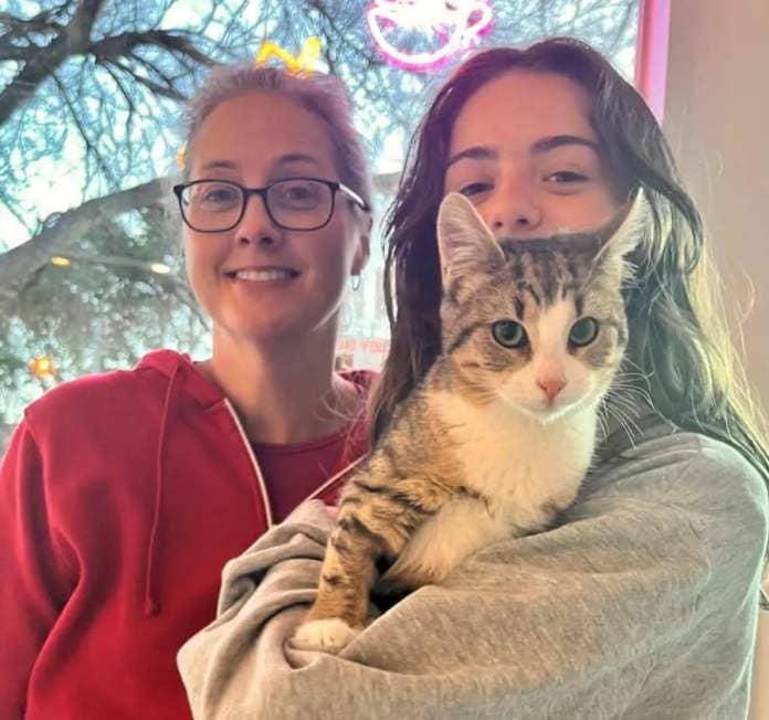 Woman in a red hoodie and another woman holding rescue cat Cotton, they have adopted. 