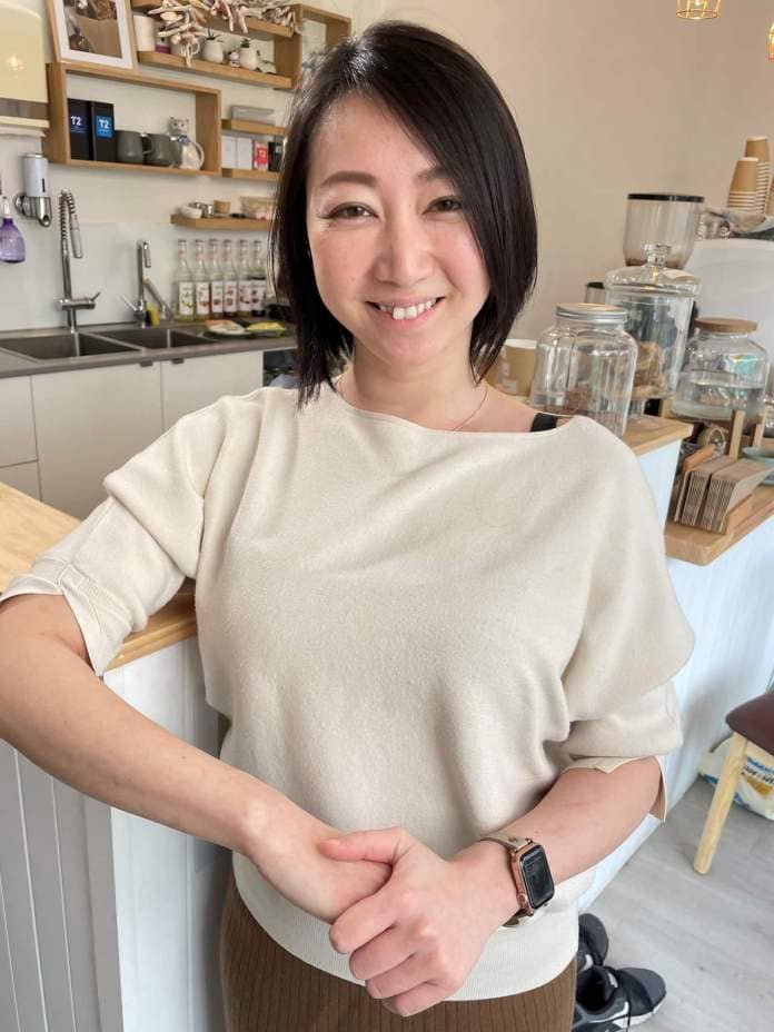 A woman with short black hair in a beige shirt standing at the counter in a cafe.