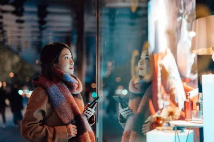 Young woman admiring window display while holiday shopping on winter evening.