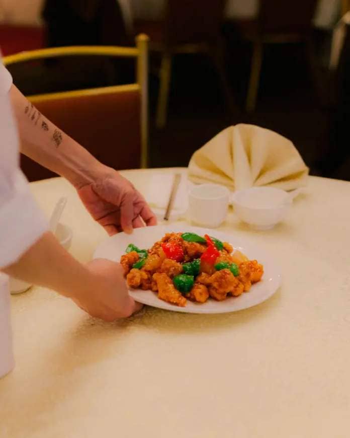 A plate of sweet and sour pork being placed on a table by a chef at Golden Paramount