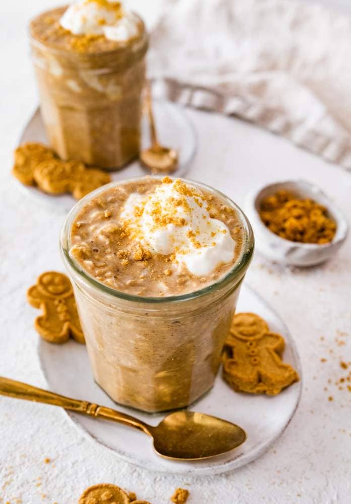 Gingerbread overnight oats in a glass cup on a small white plate with gingerbread men on it.
