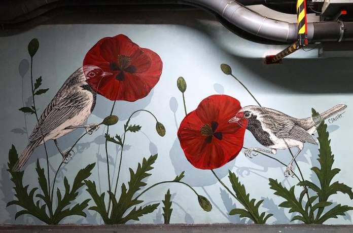 a painted acrylic mural of two birds perched in bright red floweres on a blue wall