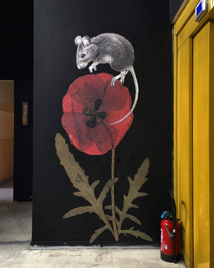 a wheatpaste of a mouse resting atop a bright red flower on a black wall