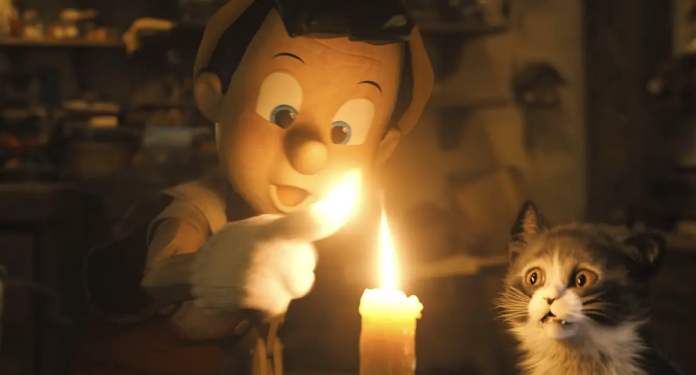 The CG version of Disney’s Pinocchio sticks his finger into a candle flame and smiles as his finger ignites, while the CG version of the cat Figaro watches with his eyes and mouth wide open in shock, in Disney’s (mostly) live-action 2022 Pinocchio