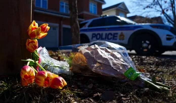 Bundles of flowers on a suburban lawn at the end of winter. A police car is in the background.