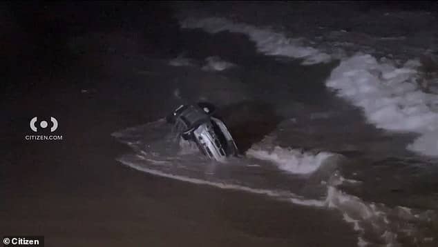 The car is seen rocking in the waves after the woman, who was being pursued by police, drove the vehicle on the sand and into the water