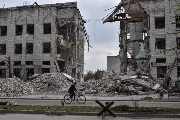 FILE - A local woman rides a bicycle on April 18, 2024, in front of a building destroyed by a Russian airstrike in the frontline town of Orikhiv, Ukraine. House Speaker Mike Johnson, R-La., putting his job on the line, relied on Democratic support this week to bring to the House floor a series of votes on $95 billion in foreign aid for Ukraine, Israel and other U.S. allies. Since President Joe Biden made the funding request in October, the Republican-controlled House has always loomed as the largest obstacle to final passage. (AP Photo/Andriy Andriyenko)