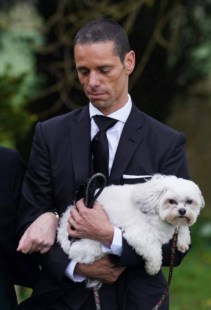 Husband of Paul O'Grady, Andre Portasio, carrying one of their dogs, arriving for the funeral of Paul O'Grady at St Rumwold's Church in Aldington, Kent. Picture date: Thursday April 20, 2023. (Photo by Gareth Fuller/PA Images via Getty Images)