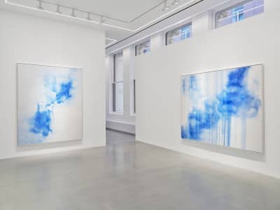 Two large paintings on white gallery walls, both with subtle modulations of blue on white canvas.