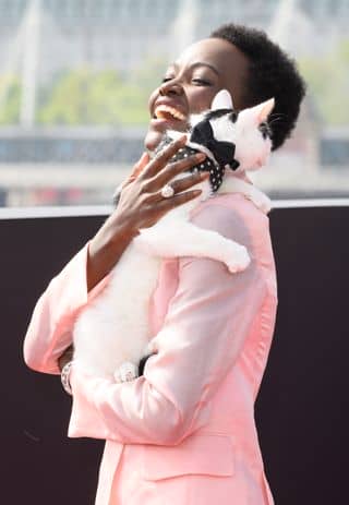 Lupita Nyong'o wearing a pink suit and holding a cat